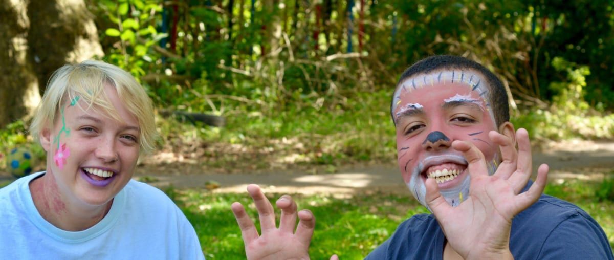 Two young people outdoors. One has face paint. Both are smiling.