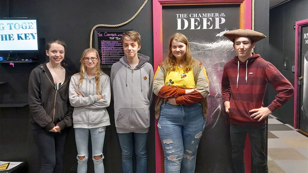 Five young people pose in front of a sign saying Secrets of the Deep.