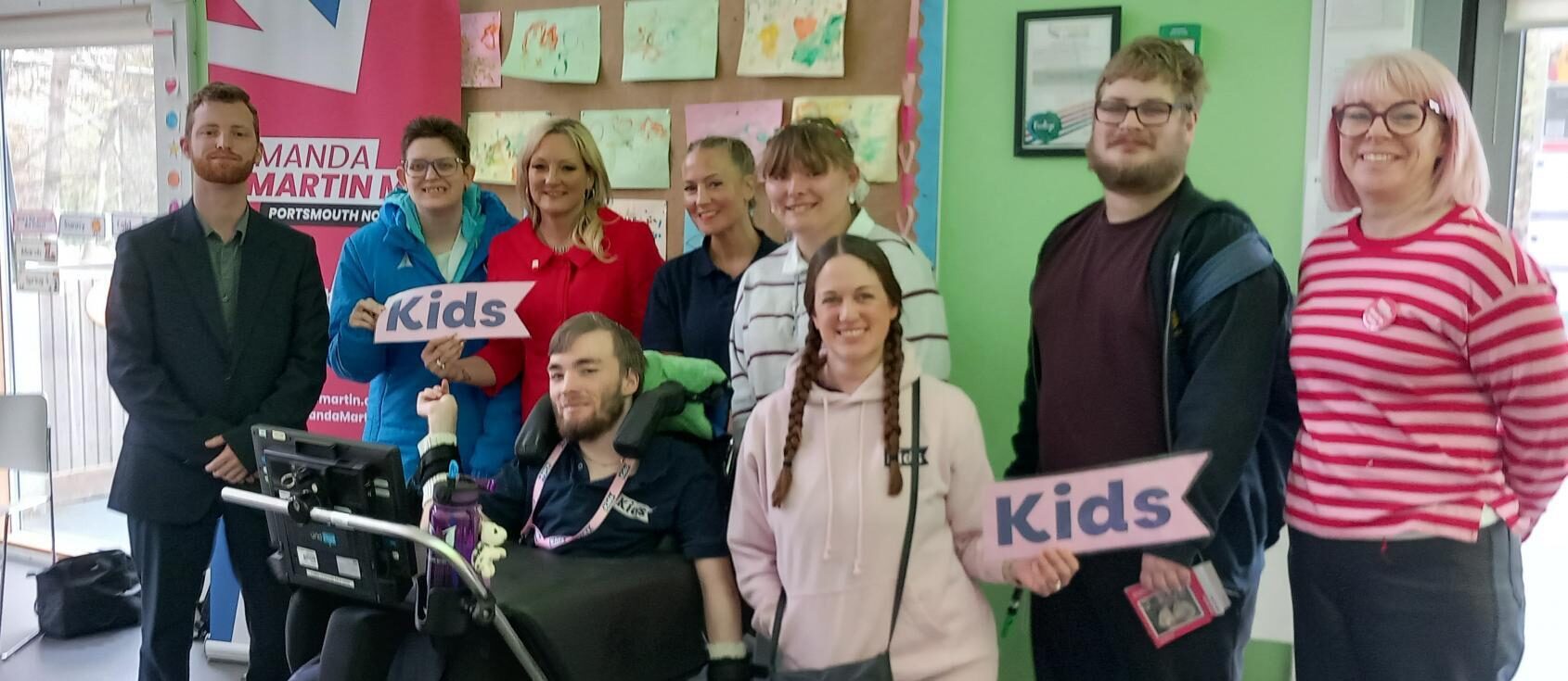 a group of disabled young people smiling and holding Kids branded signs