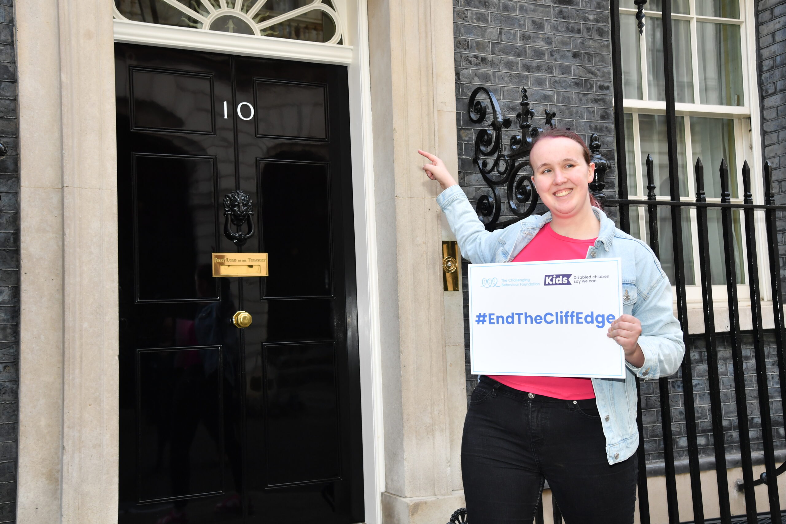 a young girl holding a banner that says end the cliff edge in front of no 10 downing street in london
